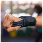 Person som bär Actimove handledsstöd i gymmiljö med knuten näve och blå söm synlig