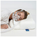 Timago CPAP kudde – kvinna sover med CPAP-mask på en vit Timago specialkudde med maskutskärningar, bild 1