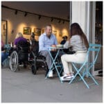 eFOLDi Navigator – hopfälld vid cafébord ger frihet och flexibilitet Man vid cafébord med hopfälld elrullstol bredvid